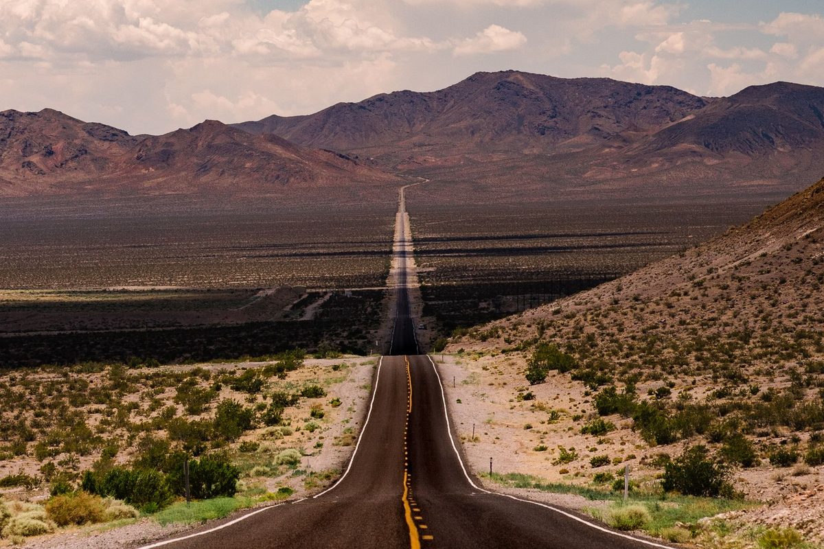 An empty two-lane highway running straight across the Nevada desert toward mountains