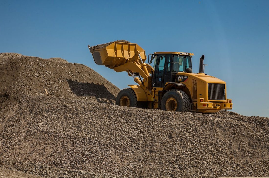 A wheel loader working on a large pile of gravel under a blue sky