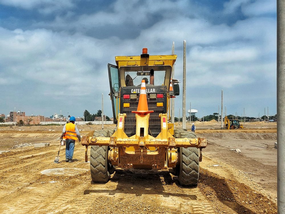 A motor grader levelling a dirt road on a bright day
