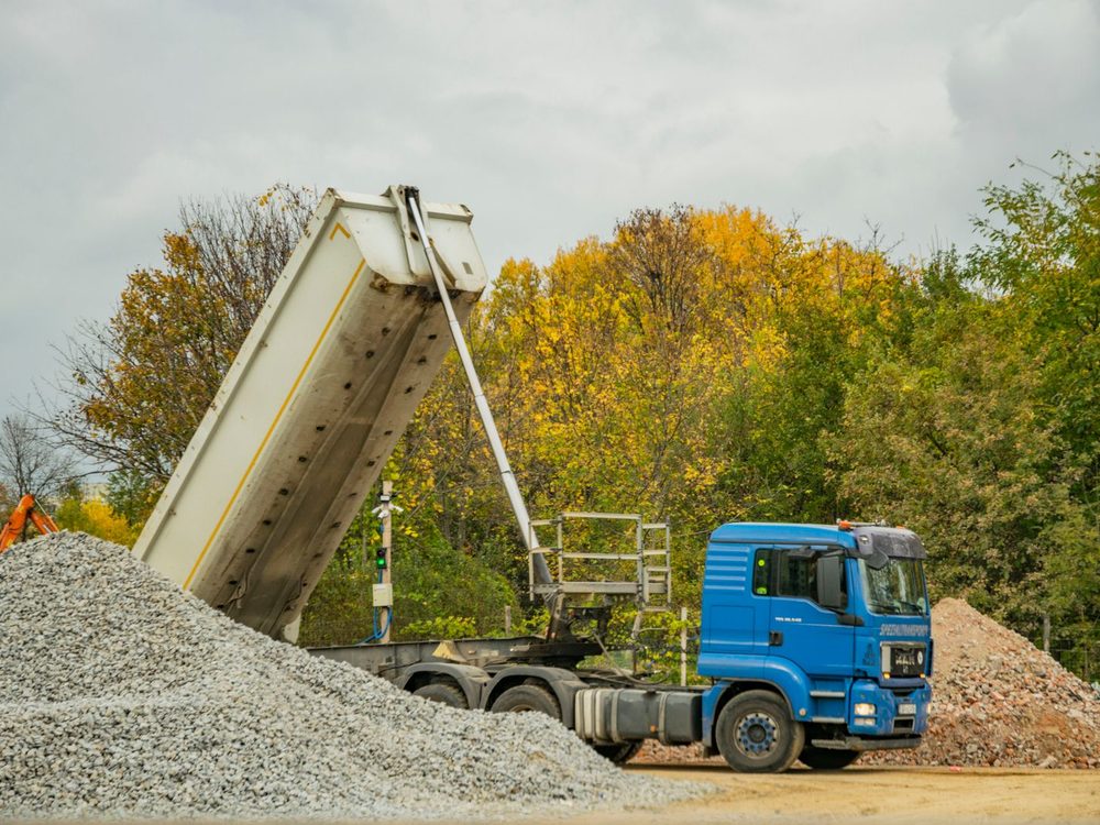 A dump truck with its bed raised, tipping a load of grey gravel into a pile
