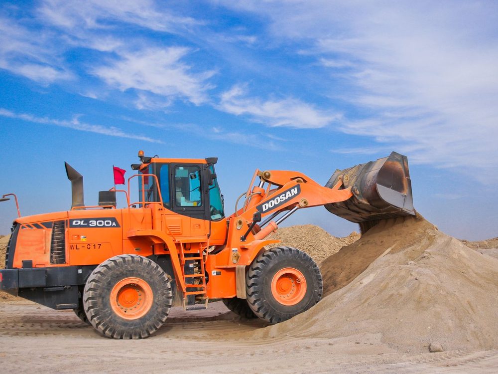 A wheel loader lifting a bucket of sand beside a sand pile
